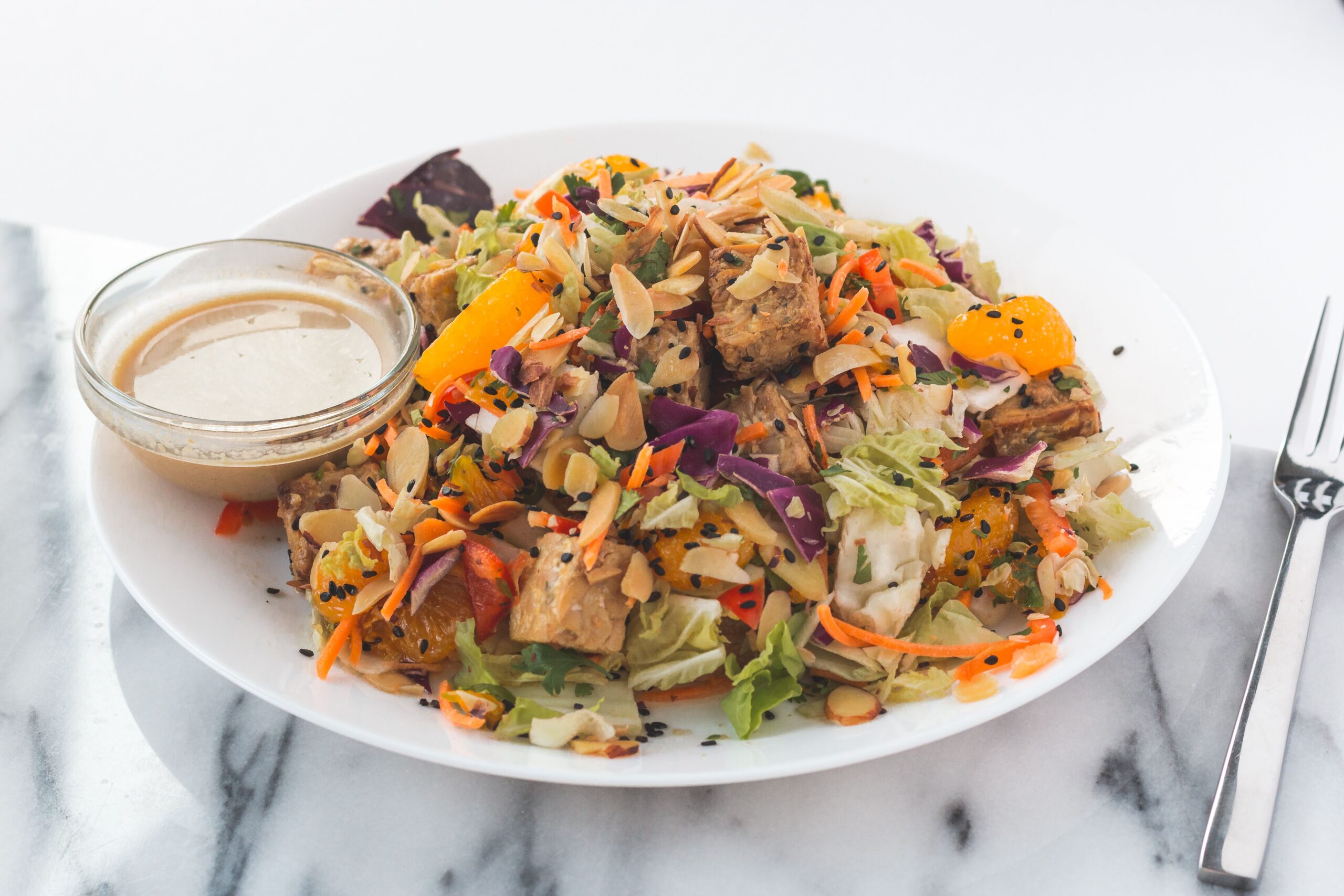 Fresh and vibrant tofu salad with orange slices, almonds, and dressing on the side.